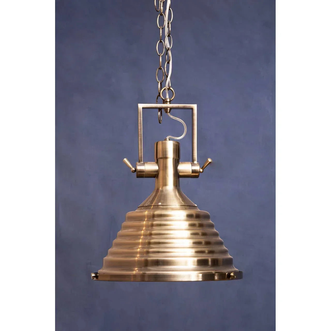 Brushed brass pendant light with ribbed metal shade and chain suspension against blue wall