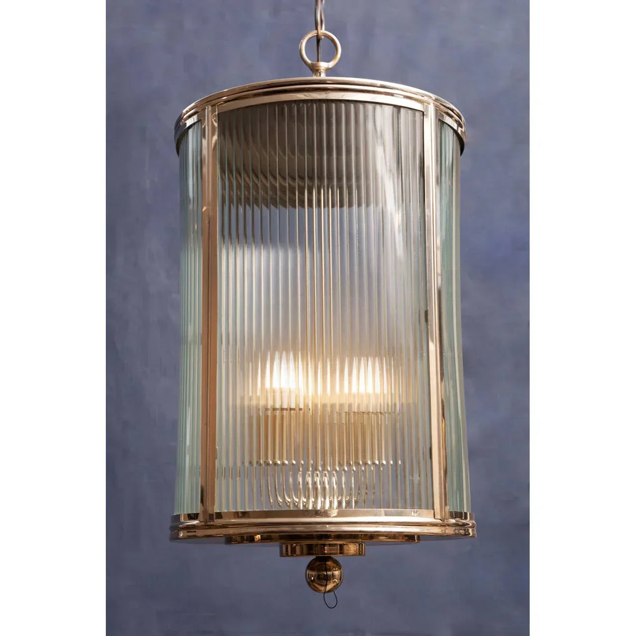 Brass and glass pendant ceiling light with ribbed cylindrical shade hanging against blue wall