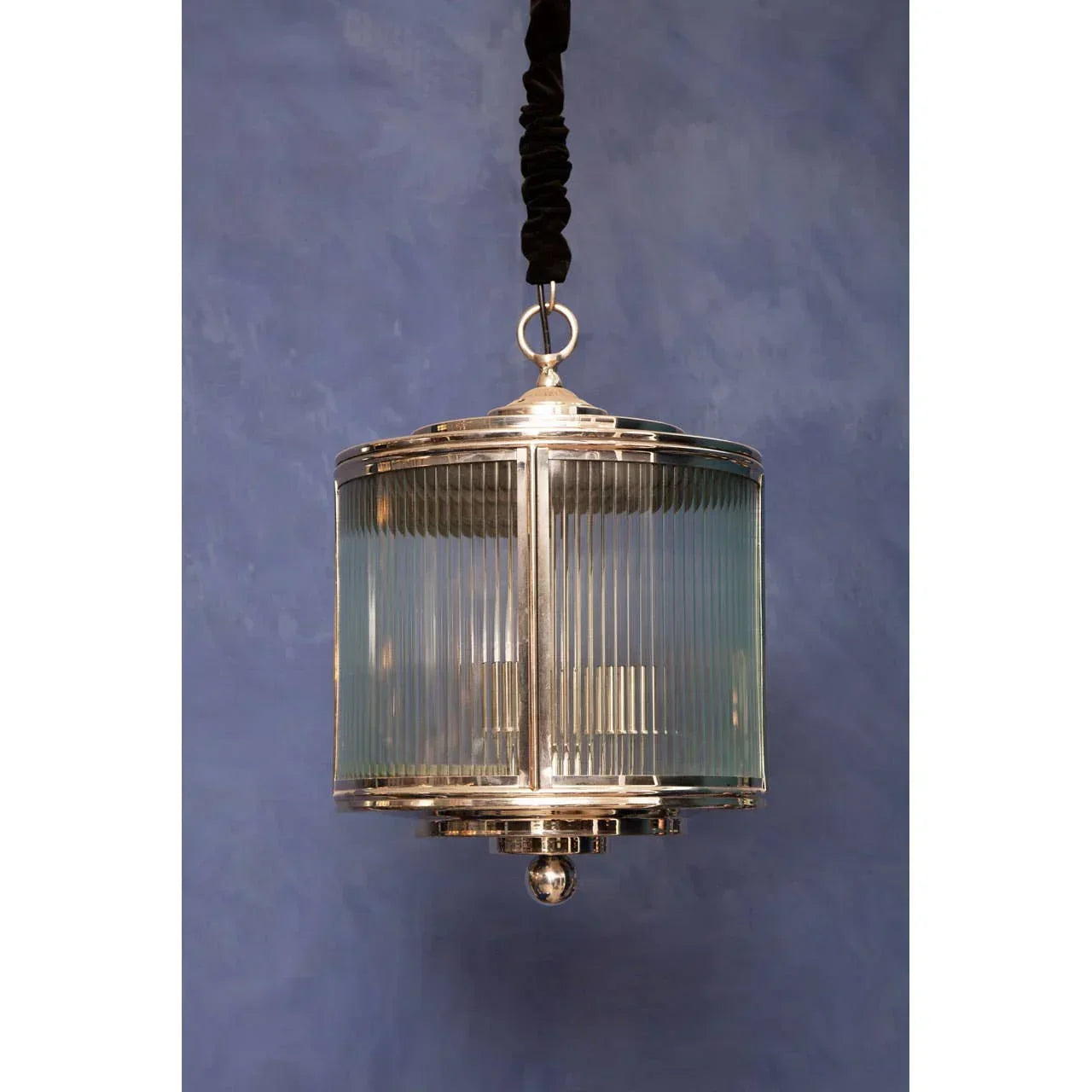 Modern pendant light with glass and chrome finish hanging against a blue wall