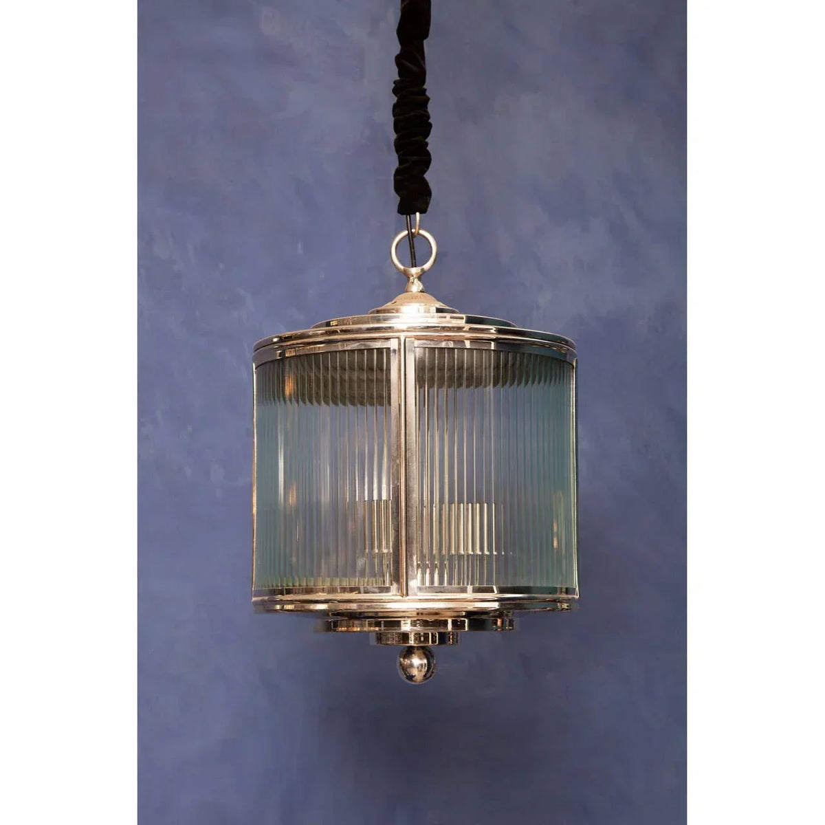 Modern pendant light with glass and chrome finish hanging against a blue wall