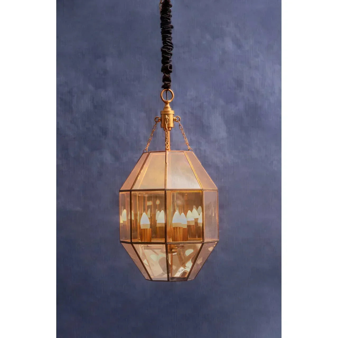 Gold geometric glass pendant light fixture with candle bulbs against blue wall