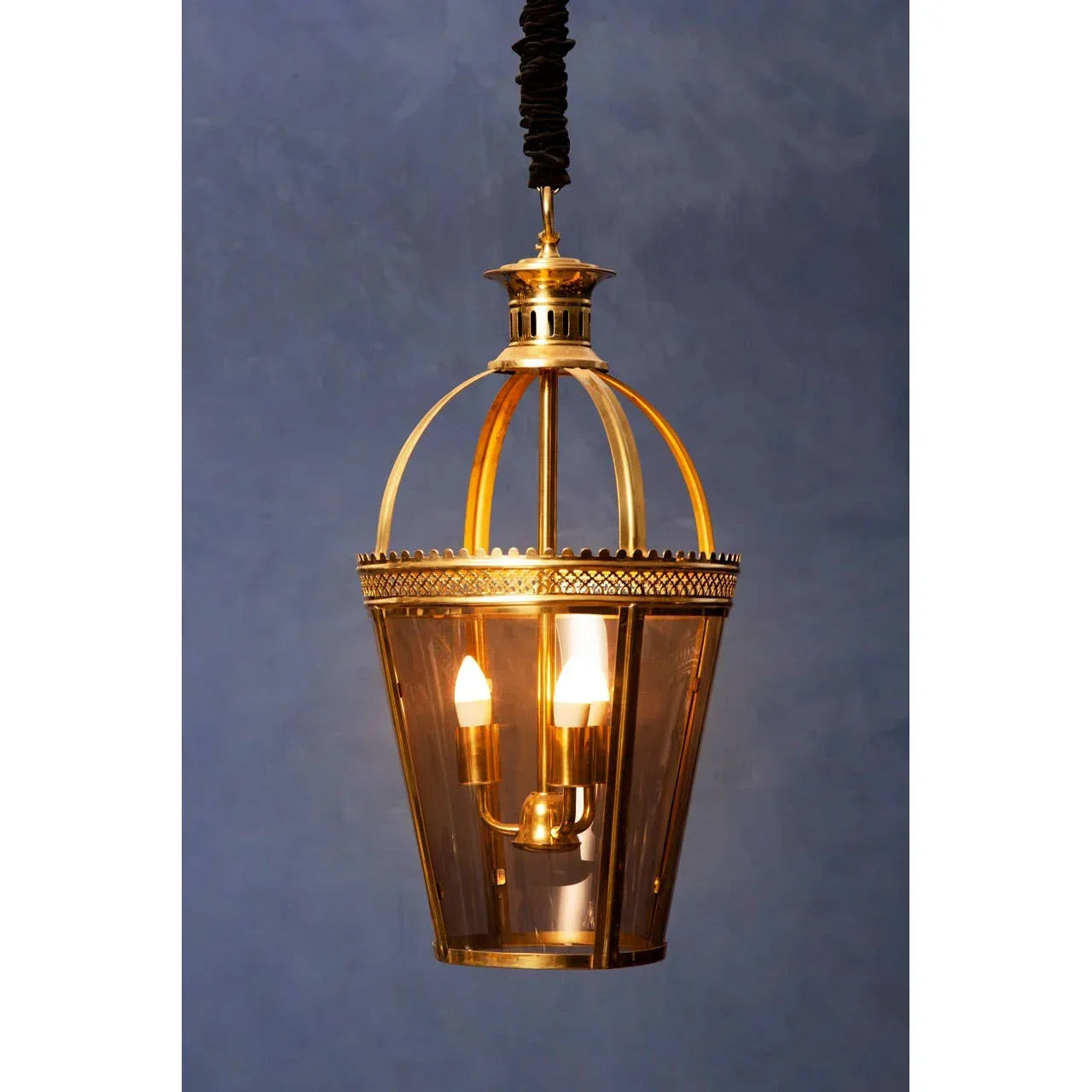 Brass pendant ceiling light with glass panels and candle-style bulbs against blue wall
