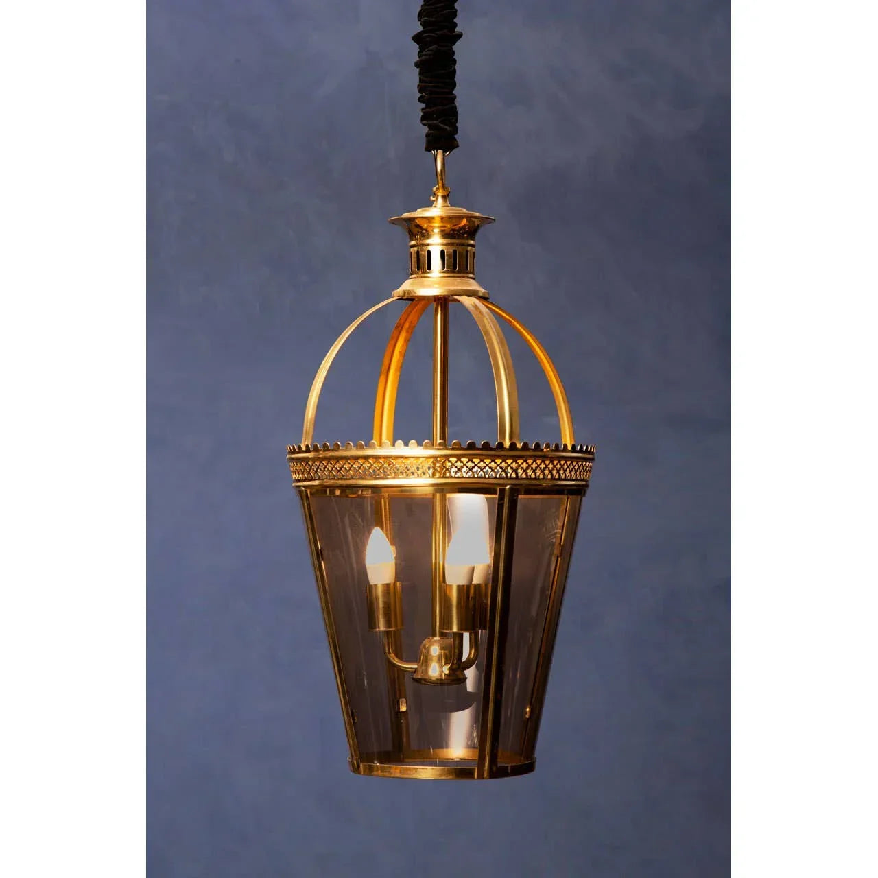Brass pendant light fixture with glass panels and candle-style bulbs against blue wall