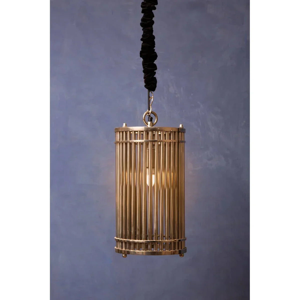Brass pendant light with cylindrical metal cage shade against blue wall