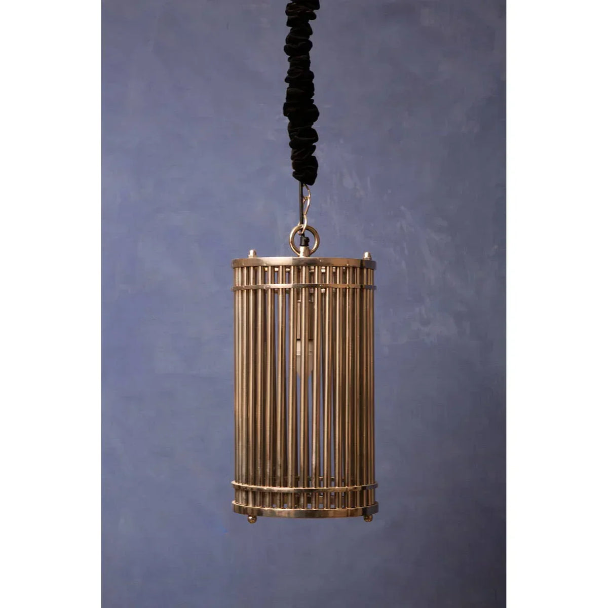 Brass pendant ceiling light with vertical metal bars on a dark fabric cord against blue wall