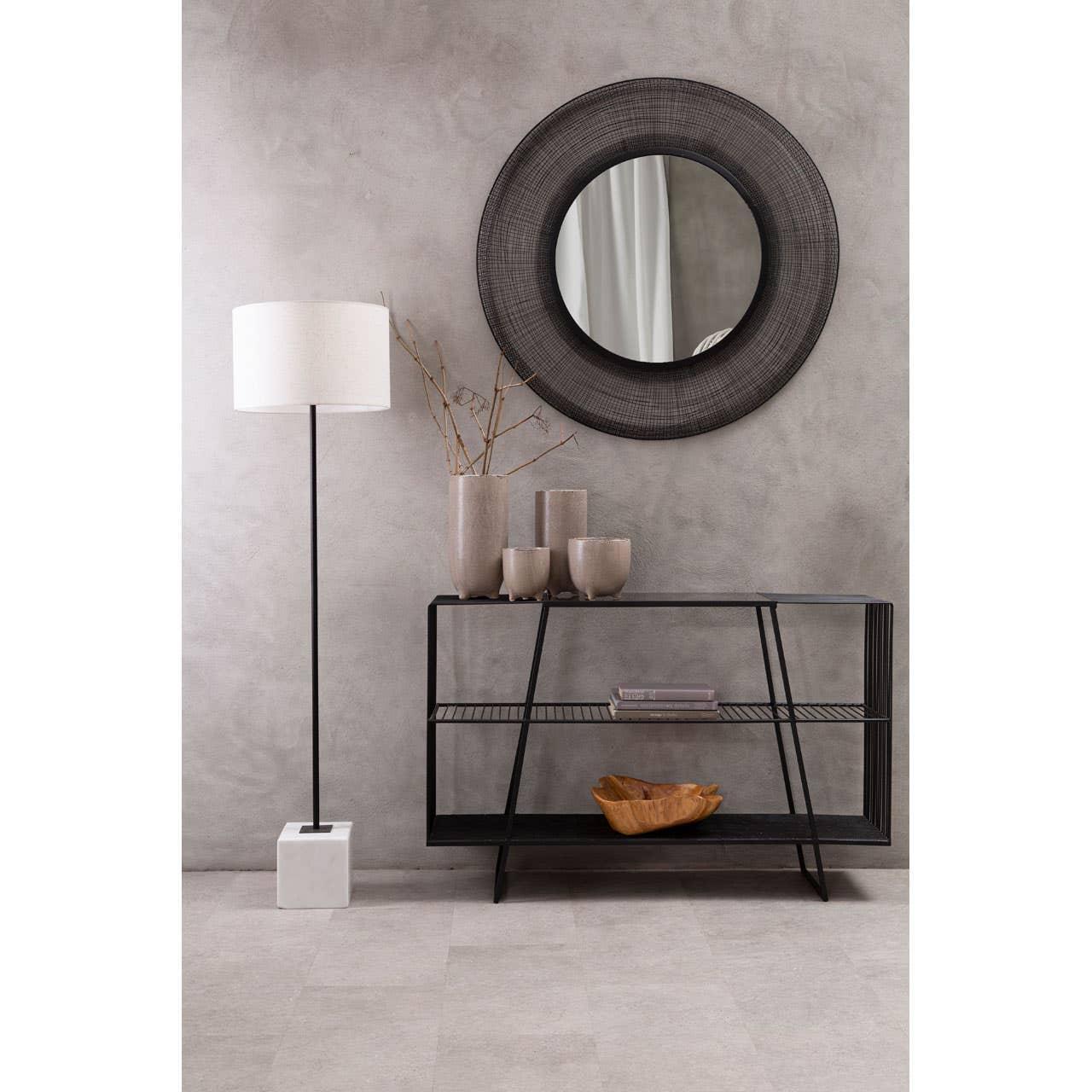 Black metal console table with ceramic vases, round wall mirror, and floor lamp in modern hallway
