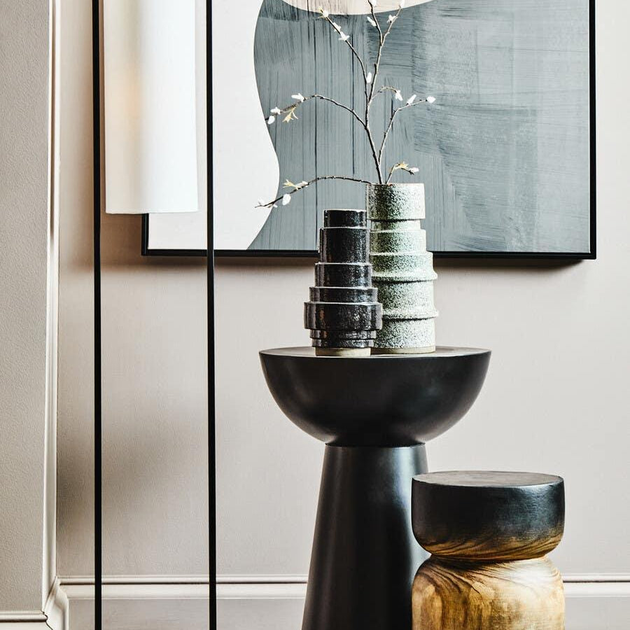 Modern floor lamp with white shade beside black side table, decorative vases, and stool