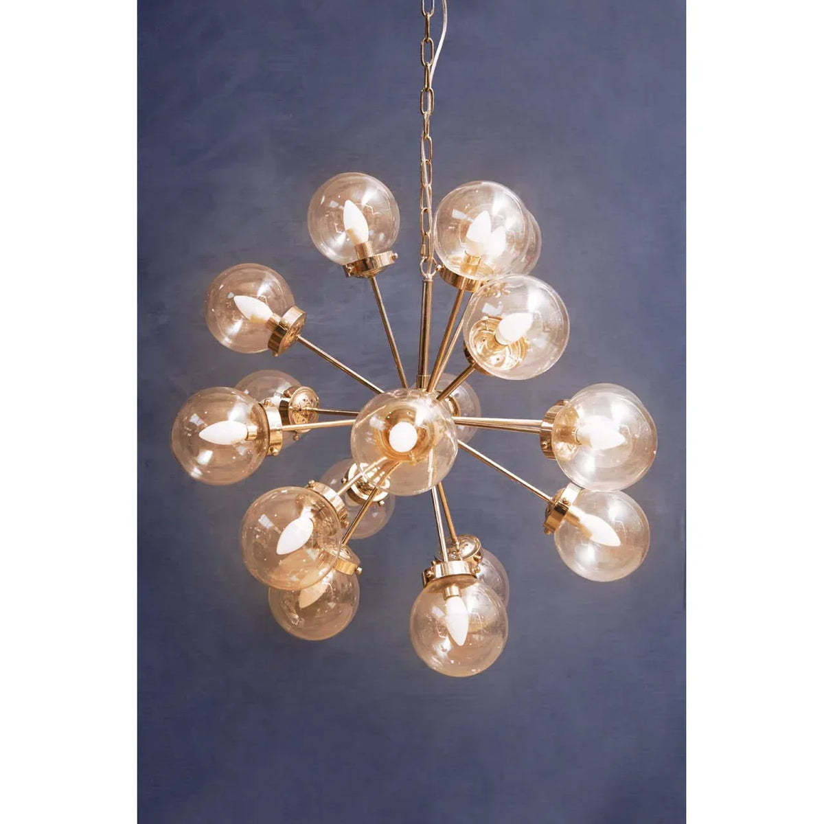 Gold sputnik chandelier with clear glass globe shades and exposed bulbs against blue wall