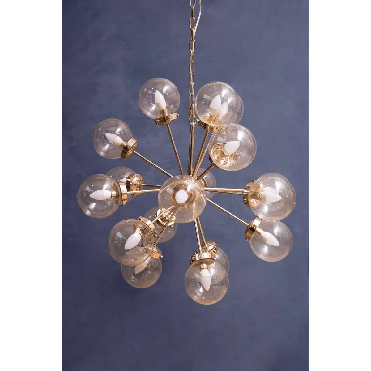 Modern gold chandelier with multiple glass globe lights against dark blue wall