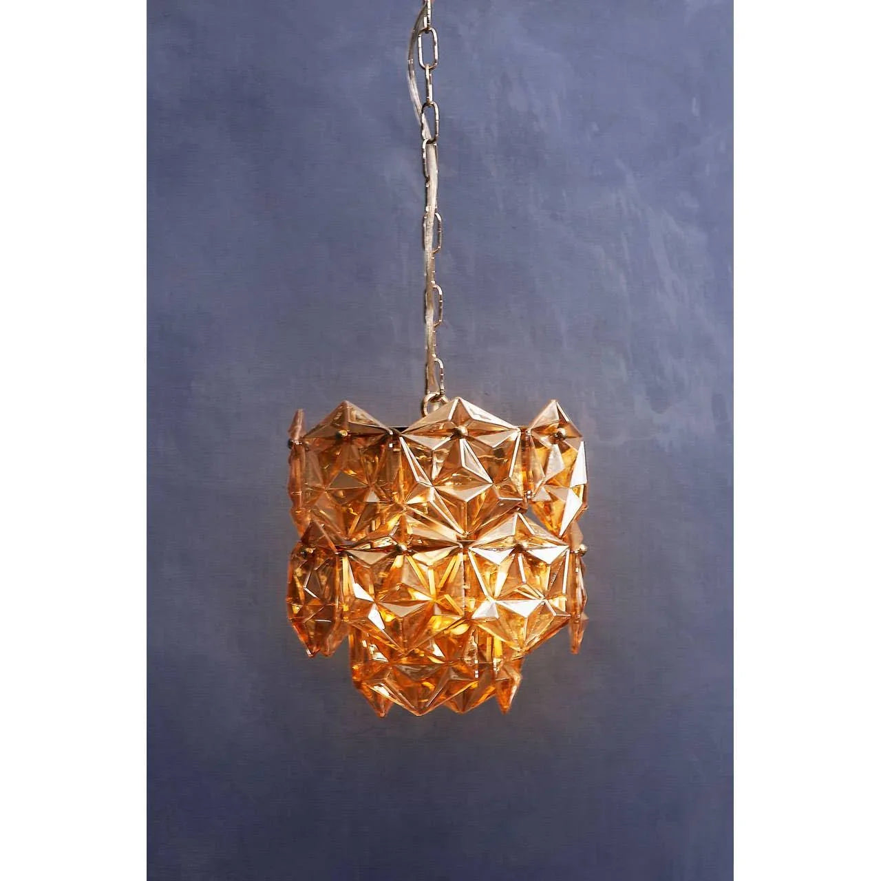 Amber glass pendant light with geometric pattern on gold chain against blue wall
