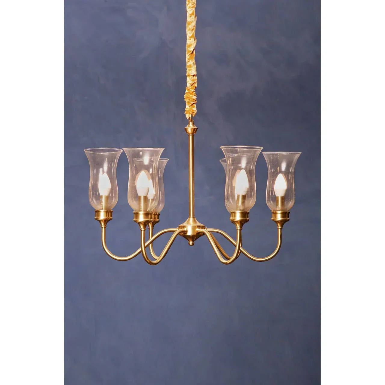 Gold chandelier with four glass lamp shades and candle-style bulbs against blue wall