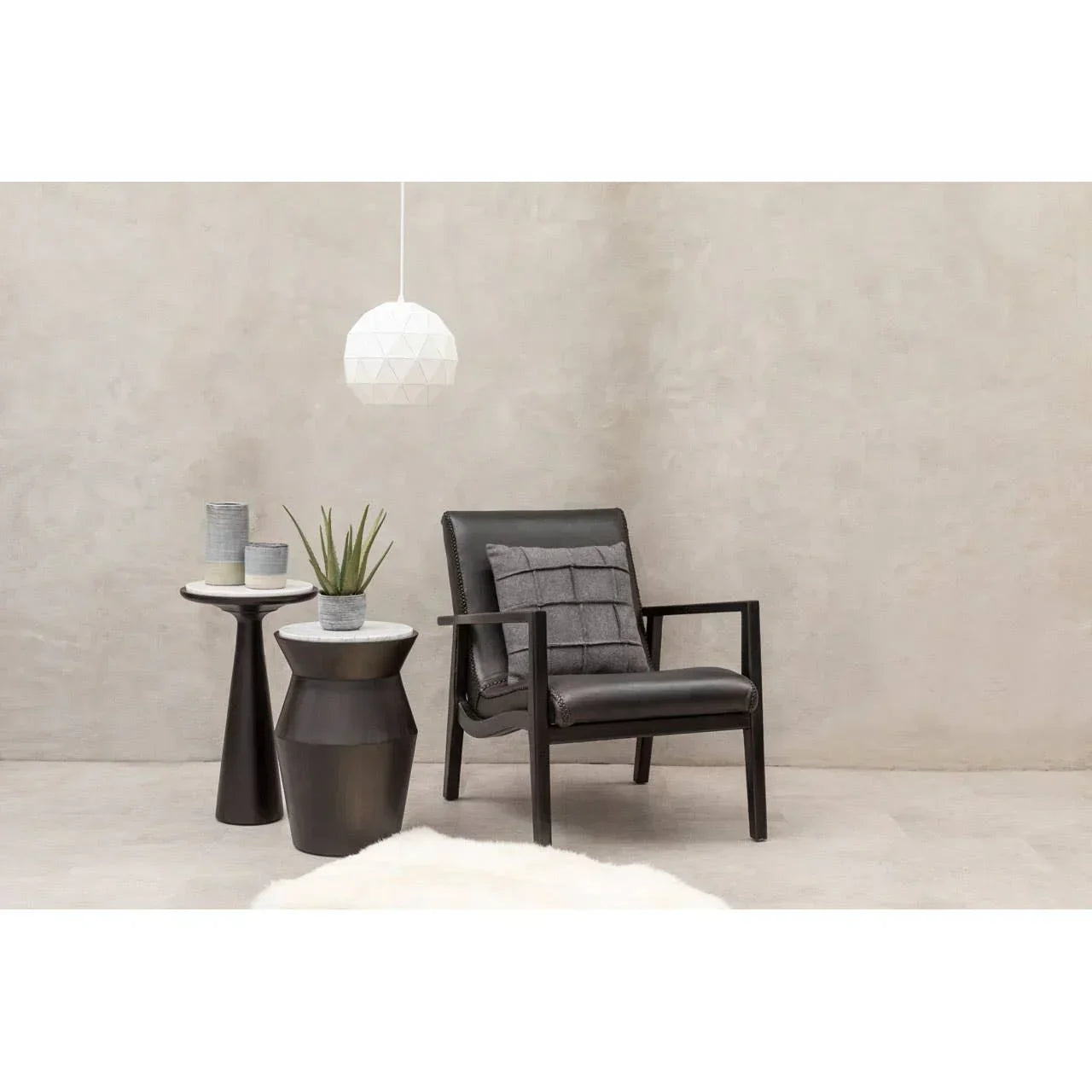 Black leather accent chair with cushion beside marble top side tables and potted plant