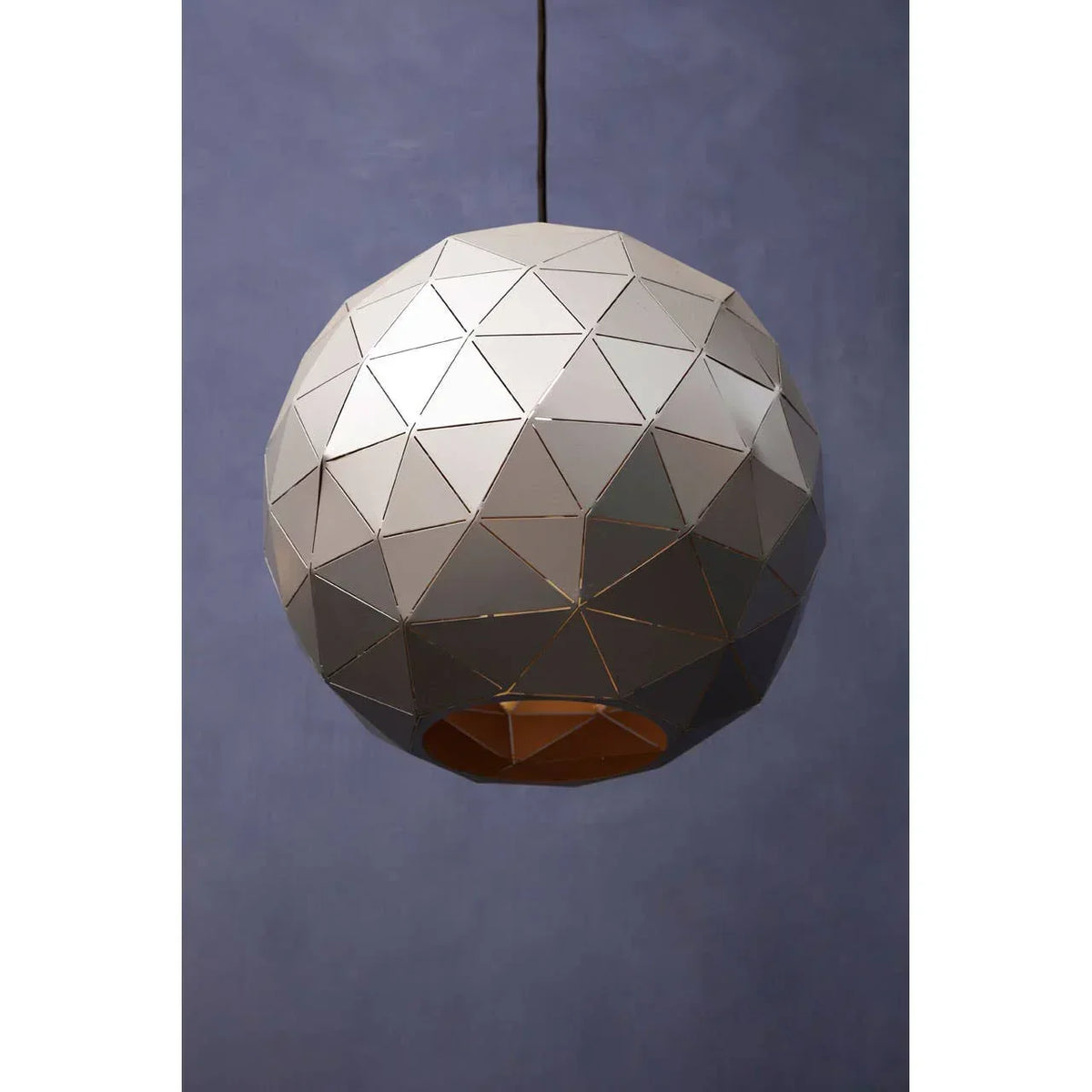 Geometric pendant light with silver metal facets suspended against a blue wall