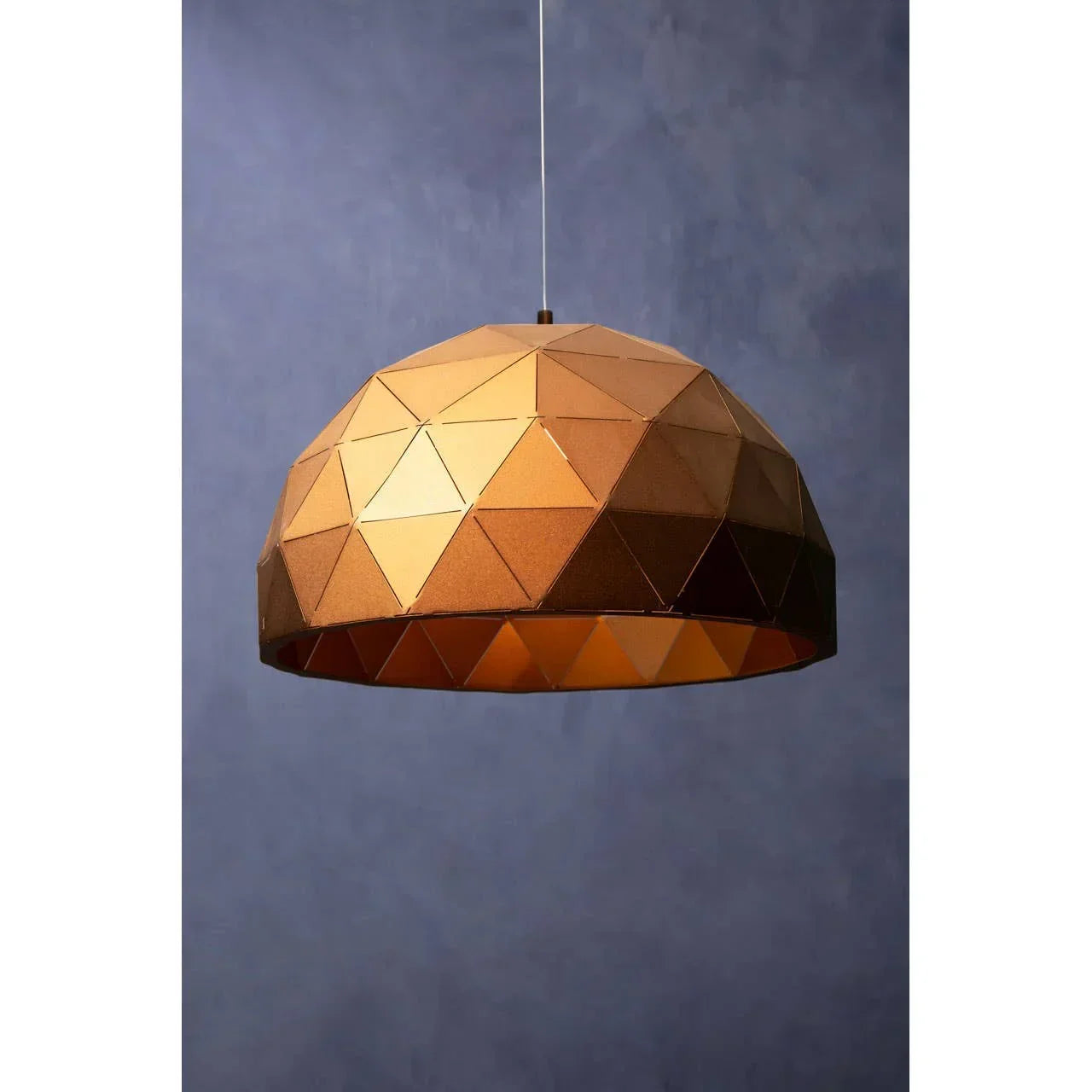 Geometric copper pendant light with faceted dome shade against a blue wall