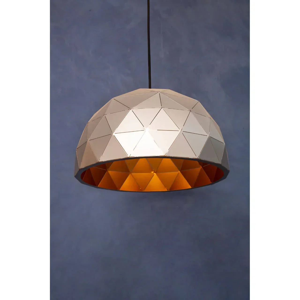 Geometric dome pendant light with metallic finish and gold interior against blue wall