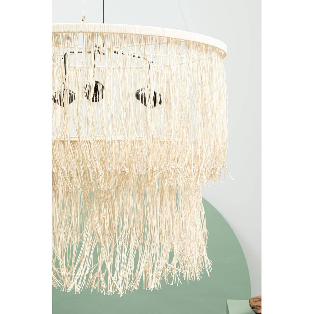 Natural rattan ceiling light with fringe detail and circular frame against pale wall
