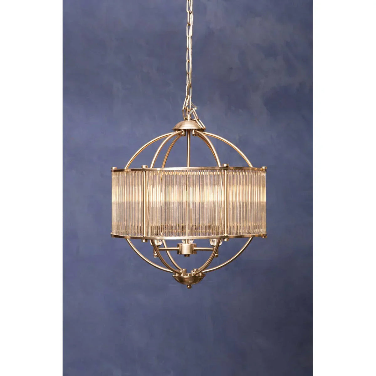 Gold metal and glass pendant light with spherical frame hanging against blue wall
