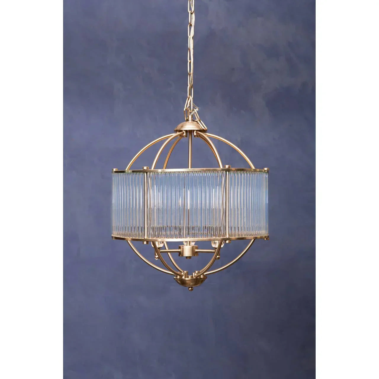 Gold and glass pendant light fixture with spherical frame against blue wall