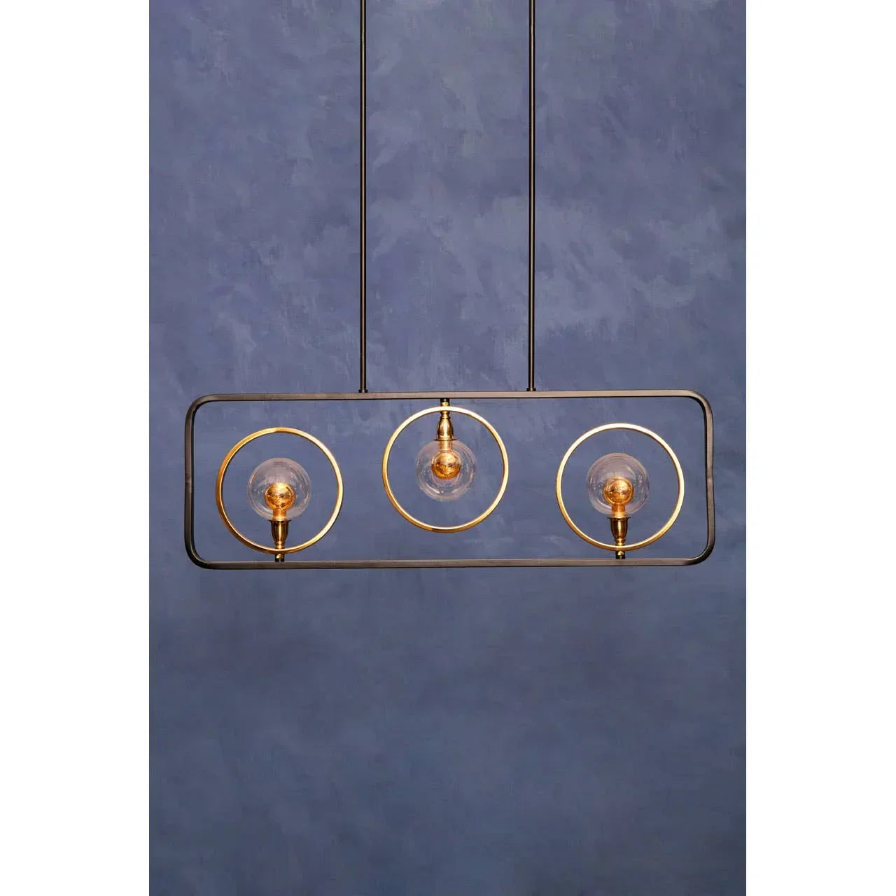 Modern pendant light with three gold rings and exposed bulbs against blue wall
