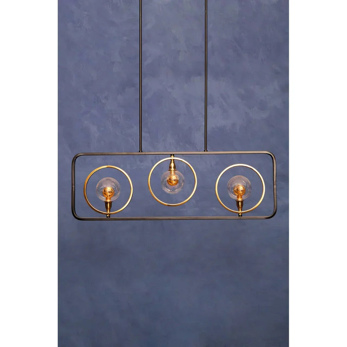 Modern pendant light with three gold rings and exposed bulbs against blue wall