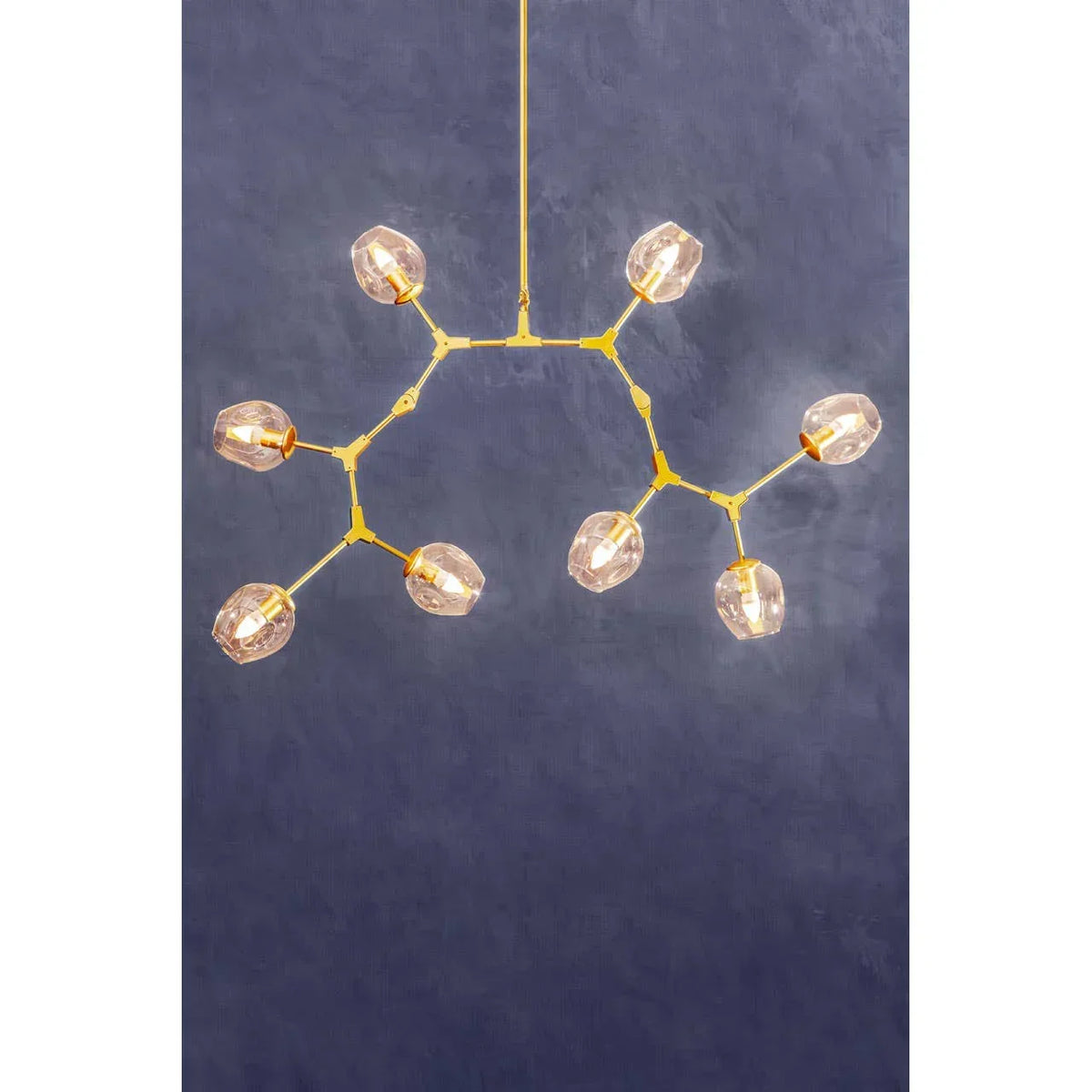 Modern gold chandelier with eight glass globe lights against a blue textured wall