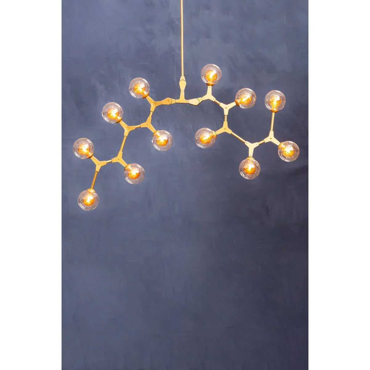 Gold modern chandelier with 14 glass globe bulbs against a dark blue wall