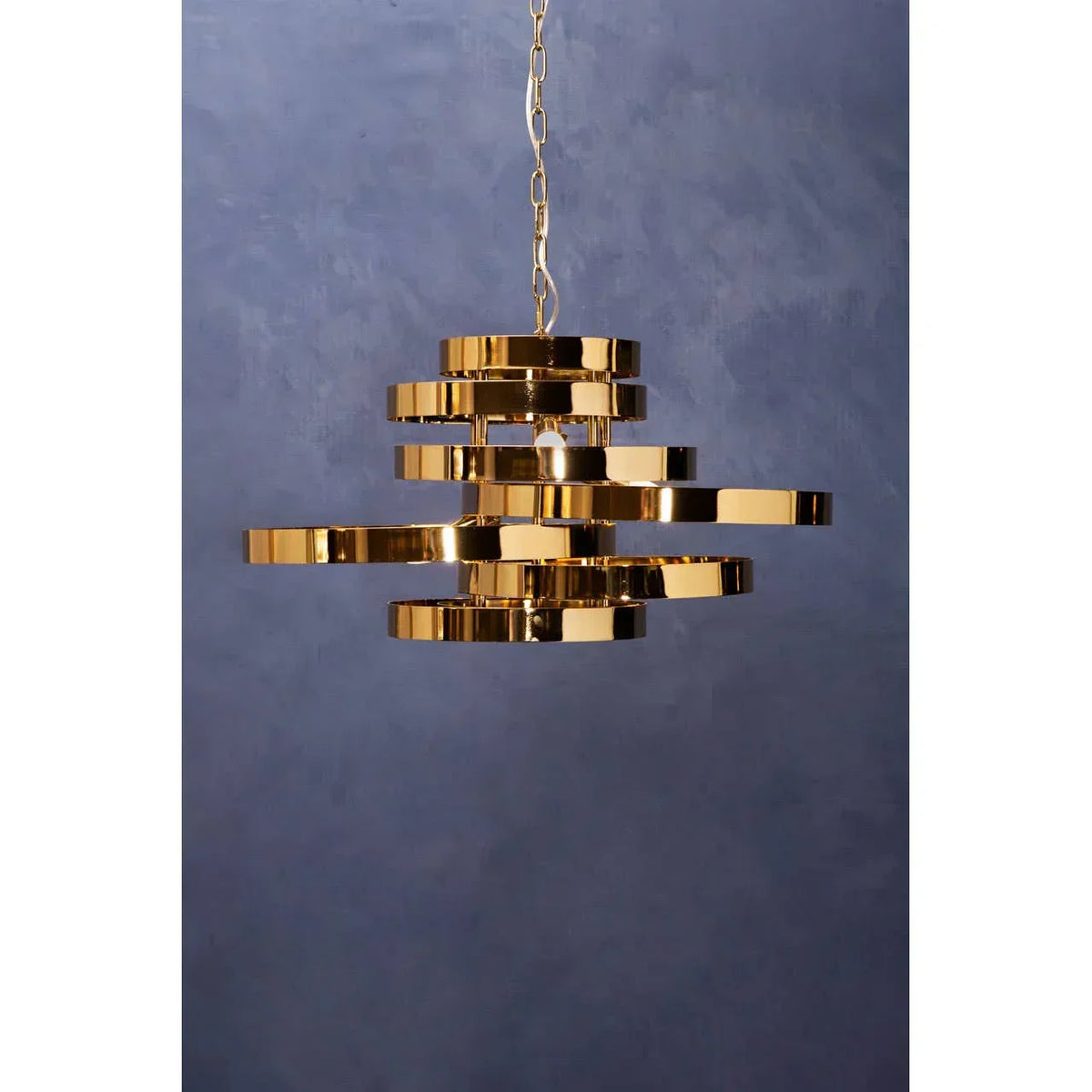 Modern gold pendant light with layered metal rings hanging against blue wall