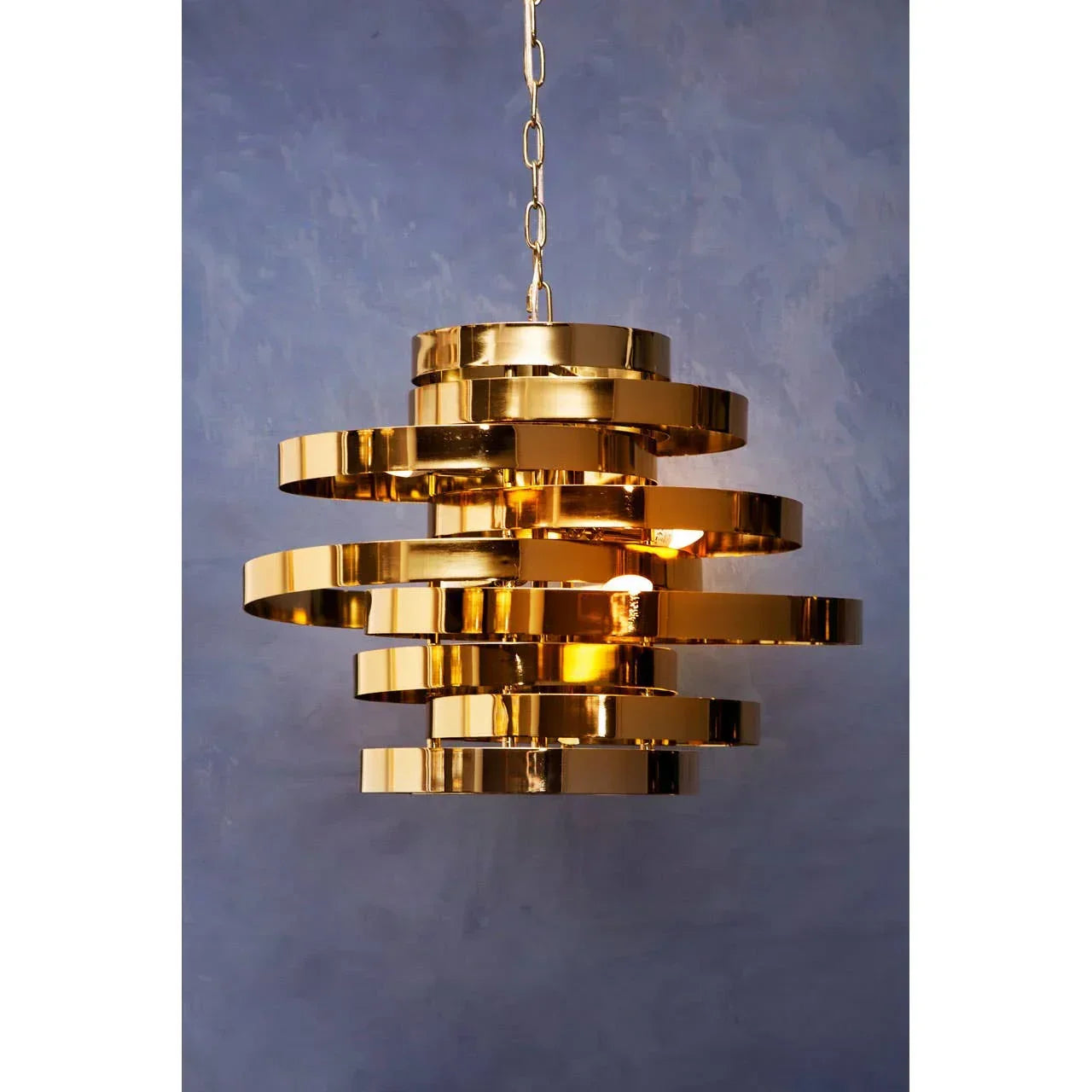 Gold metal pendant light with layered rings and central bulb against blue wall