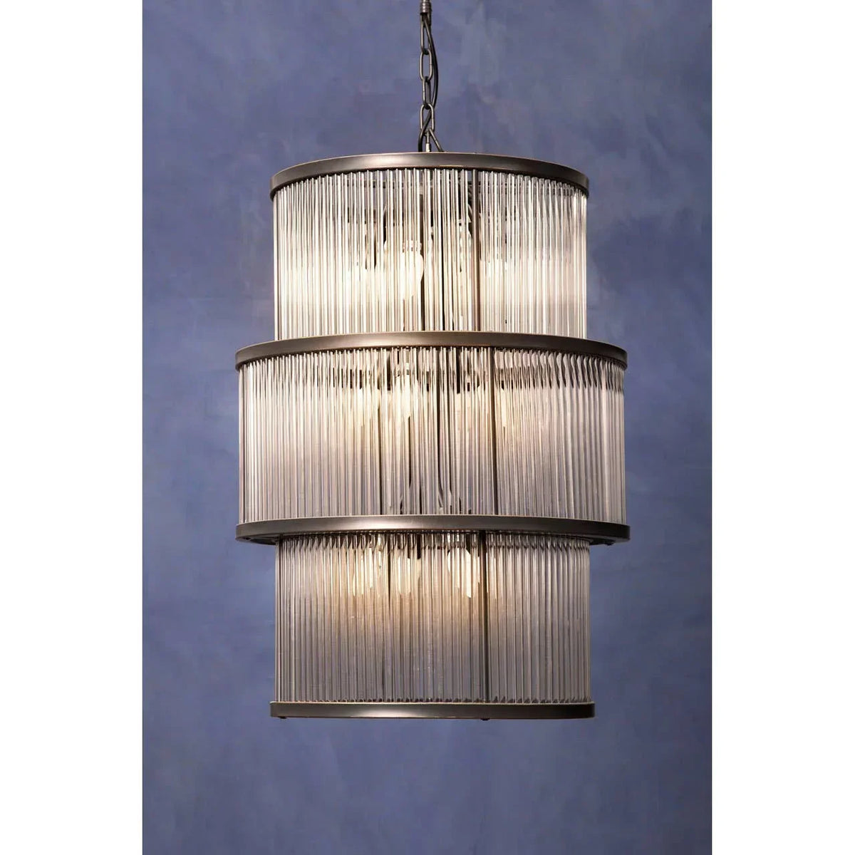 Three tier glass rod chandelier with metal frame hanging against blue wall