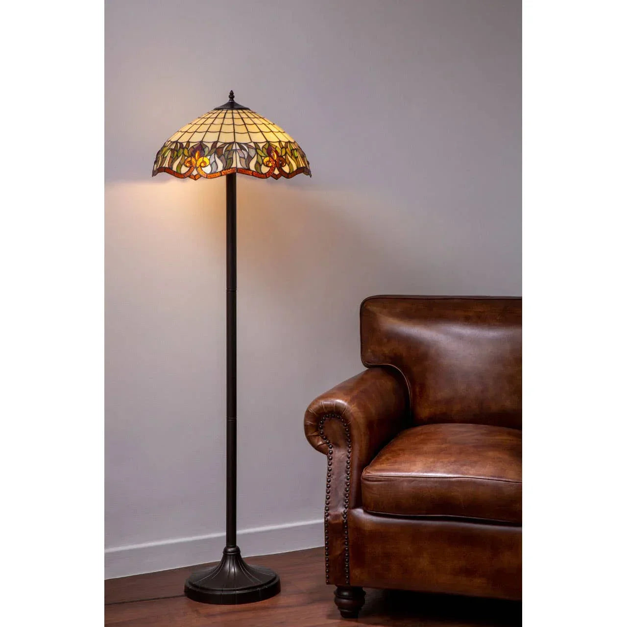 Tiffany style stained glass floor lamp beside brown leather armchair on wooden floor