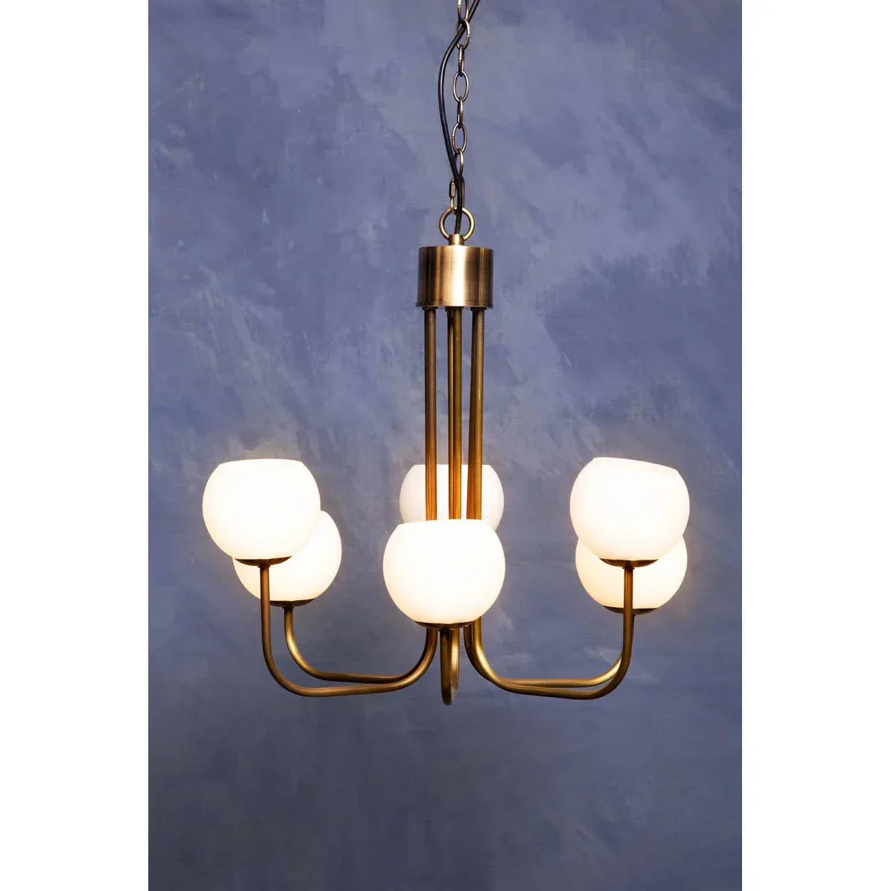 Modern brass chandelier with six white glass shades against blue wall