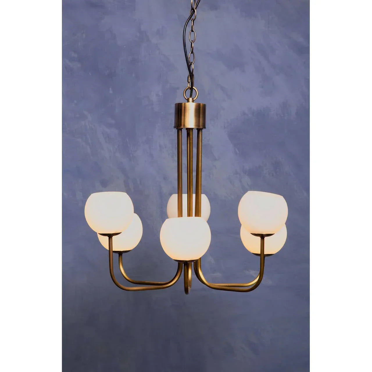Brass chandelier with five frosted glass shades against a textured blue wall background