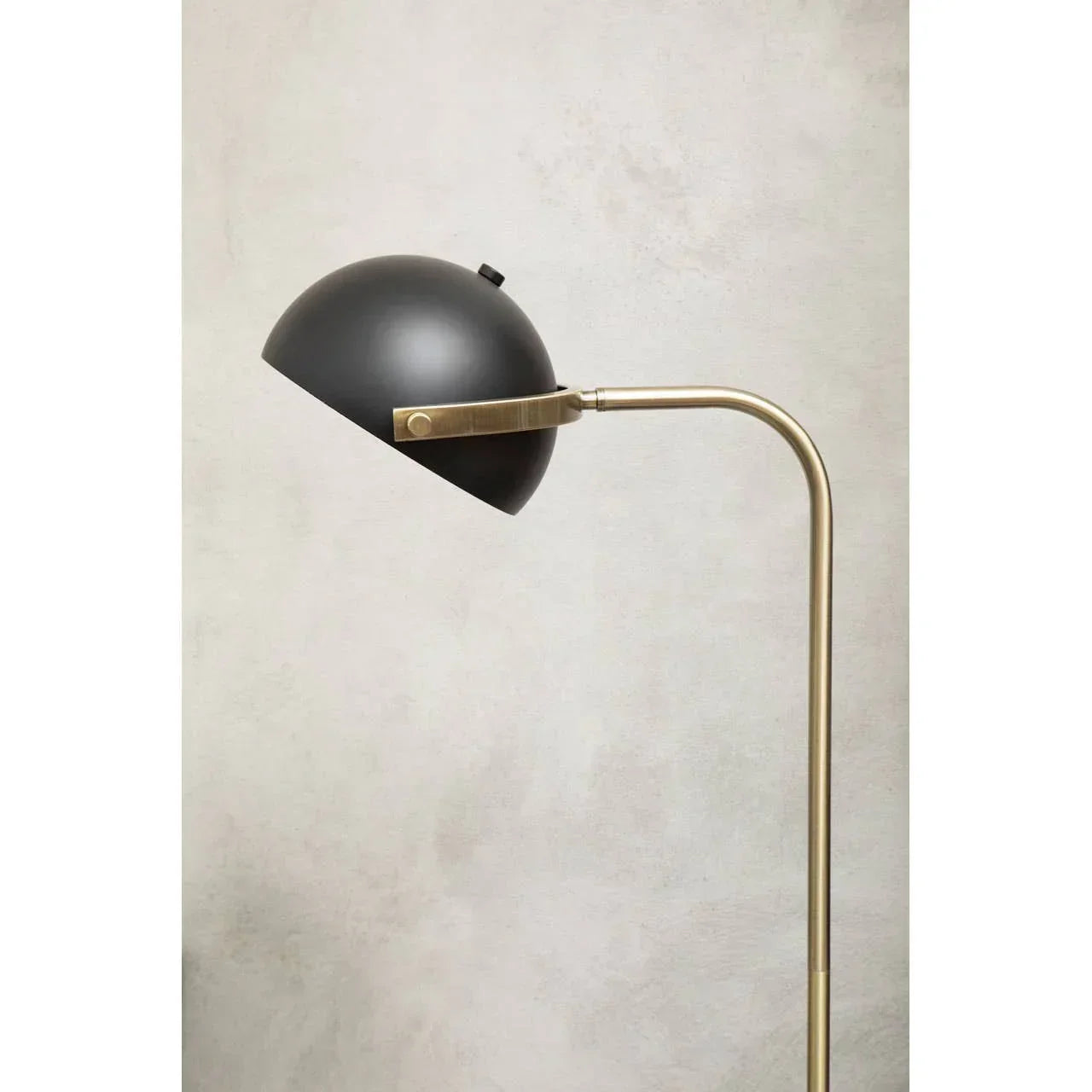 Black metal floor lamp with dome shade and brass stem against light wall