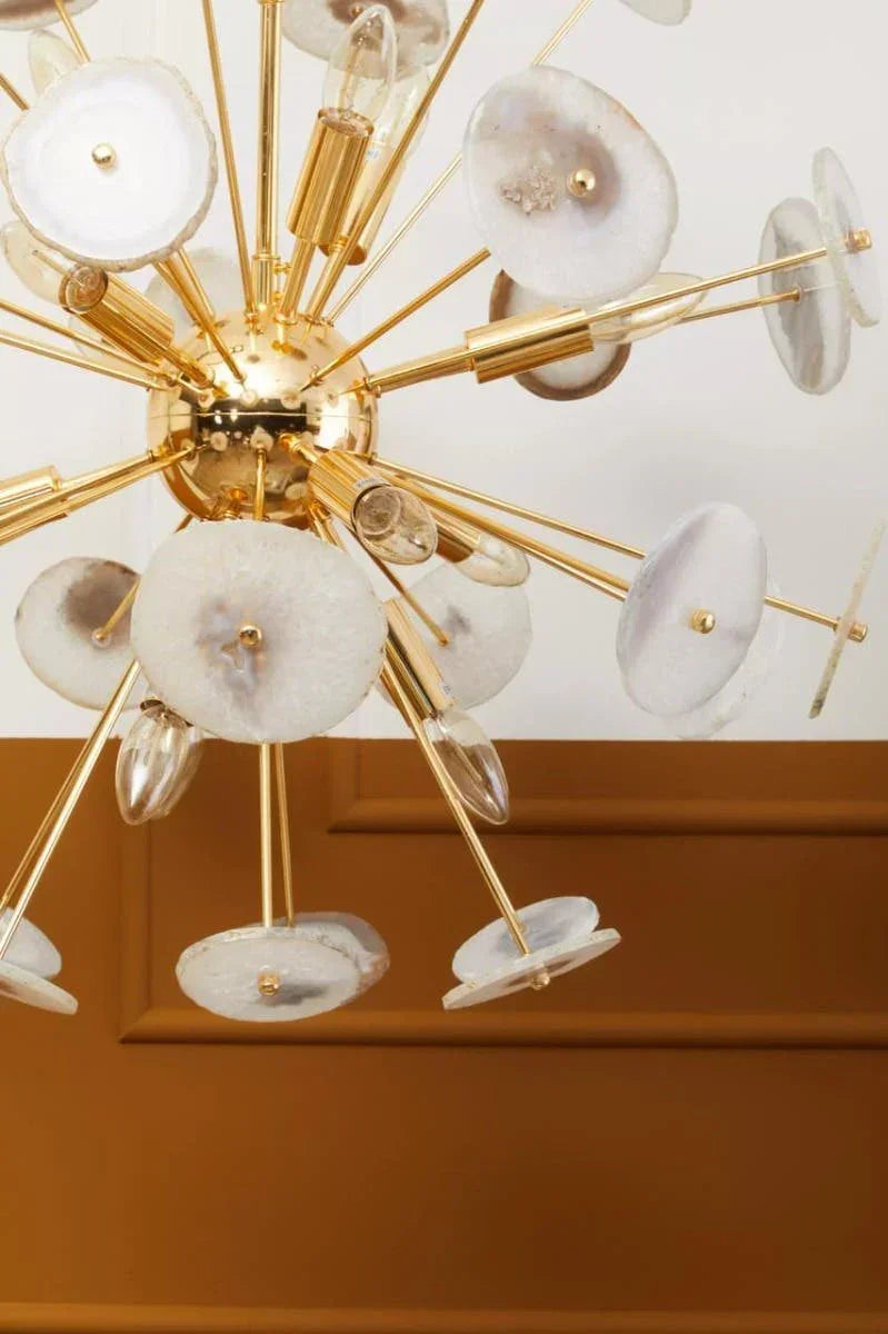 Modern gold chandelier with round crystal accents and exposed bulbs against a paneled wall