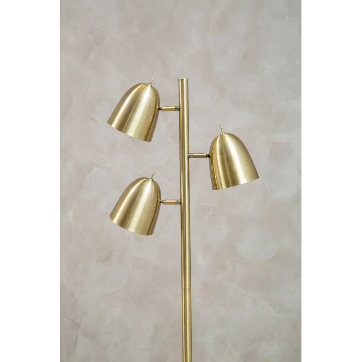 Brass floor lamp with three adjustable dome shades against neutral textured wall