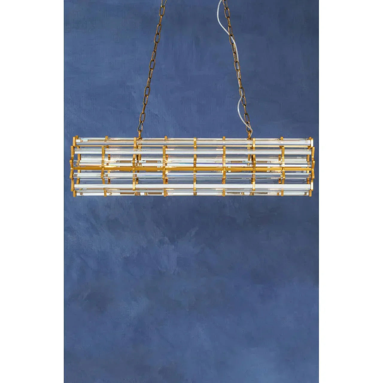 Gold and glass linear pendant light with chain suspension against blue background