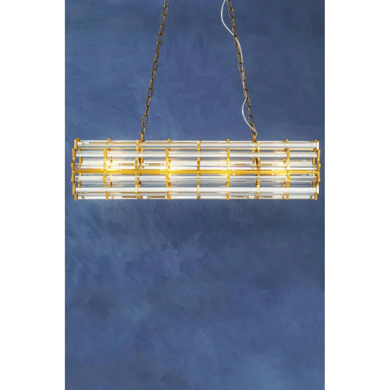 Gold and glass linear chandelier pendant light with chain against blue wall