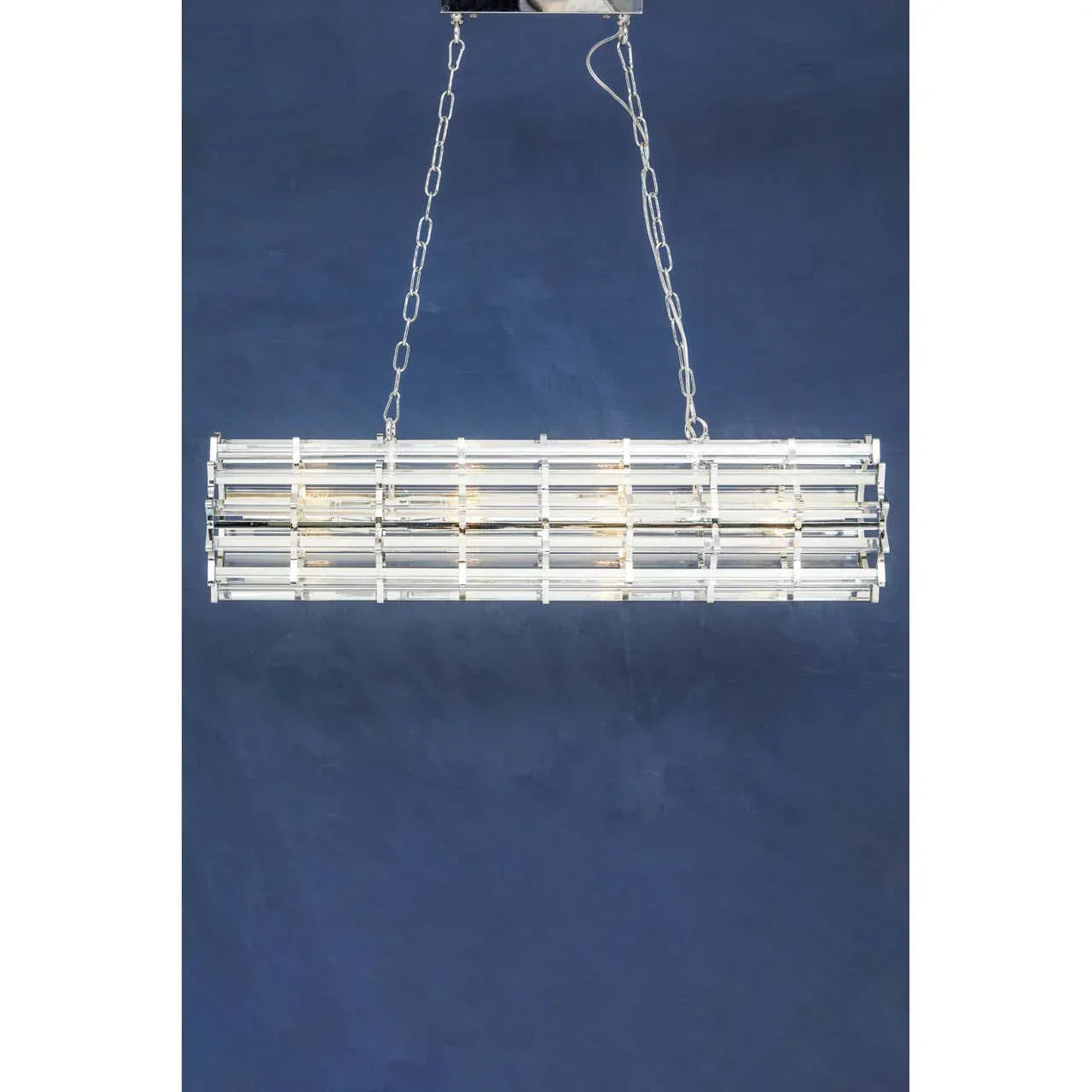 Rectangular crystal chandelier with chrome frame suspended by chains against blue wall