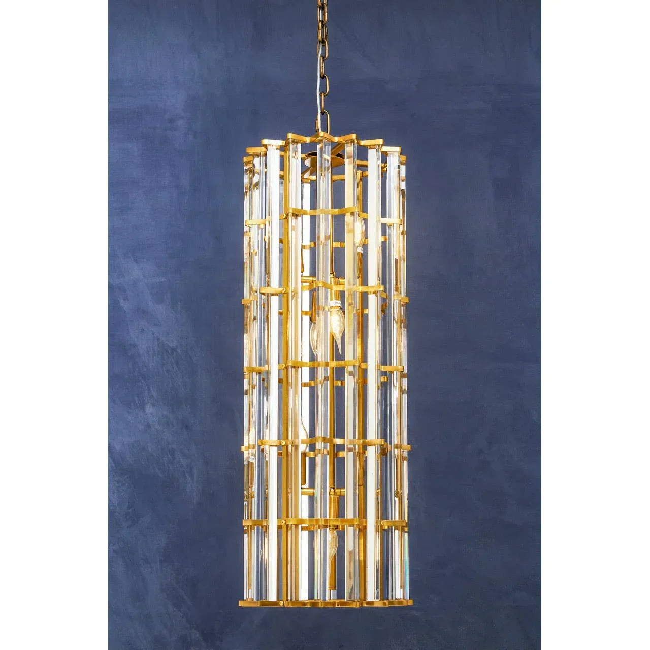 Gold and glass pendant light with vertical rods hanging against dark blue wall