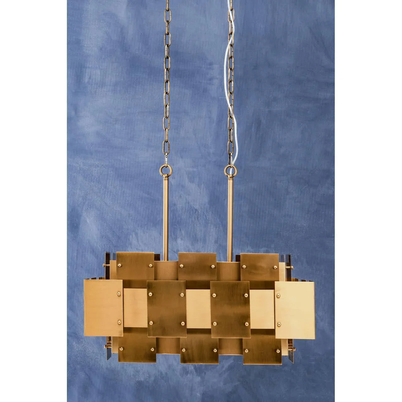 Brushed brass pendant light with geometric panels and chain suspension against blue wall