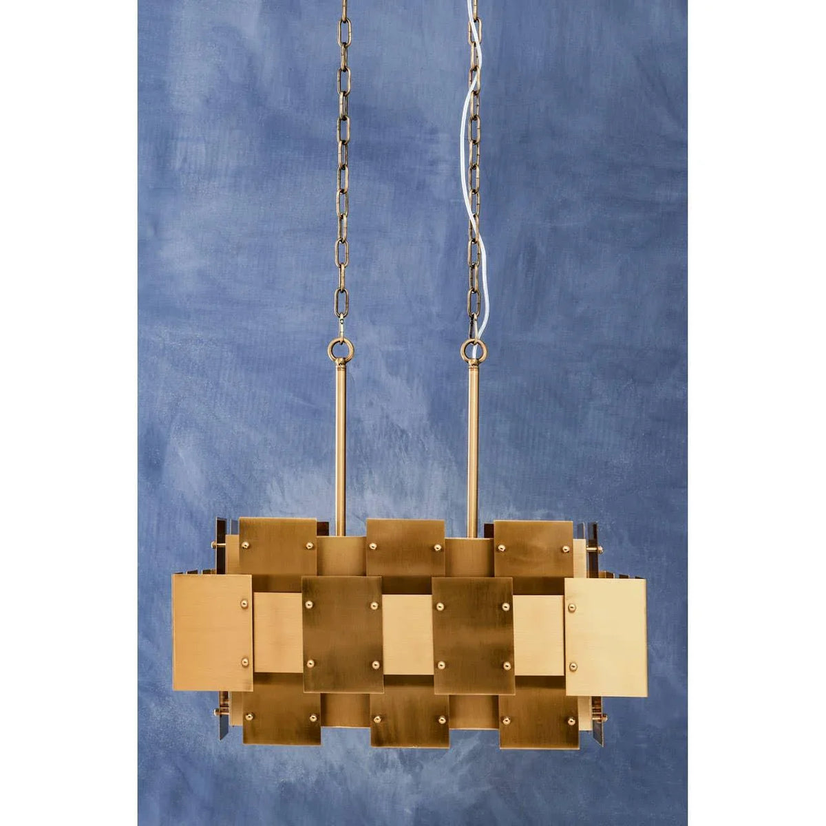Brass geometric pendant light with rectangular panels on gold chains against blue wall