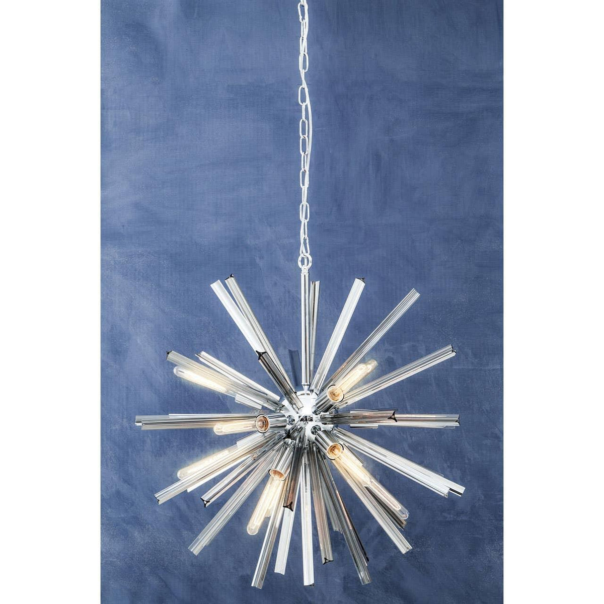 Modern starburst chandelier with chrome finish and exposed bulbs against blue wall