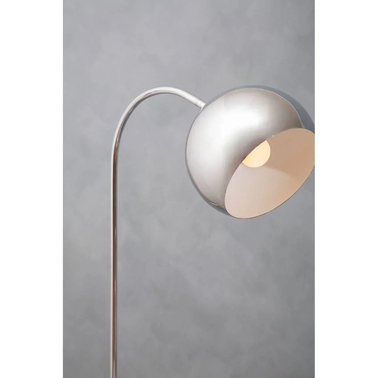 Silver floor lamp with curved stand and dome shade against grey wall
