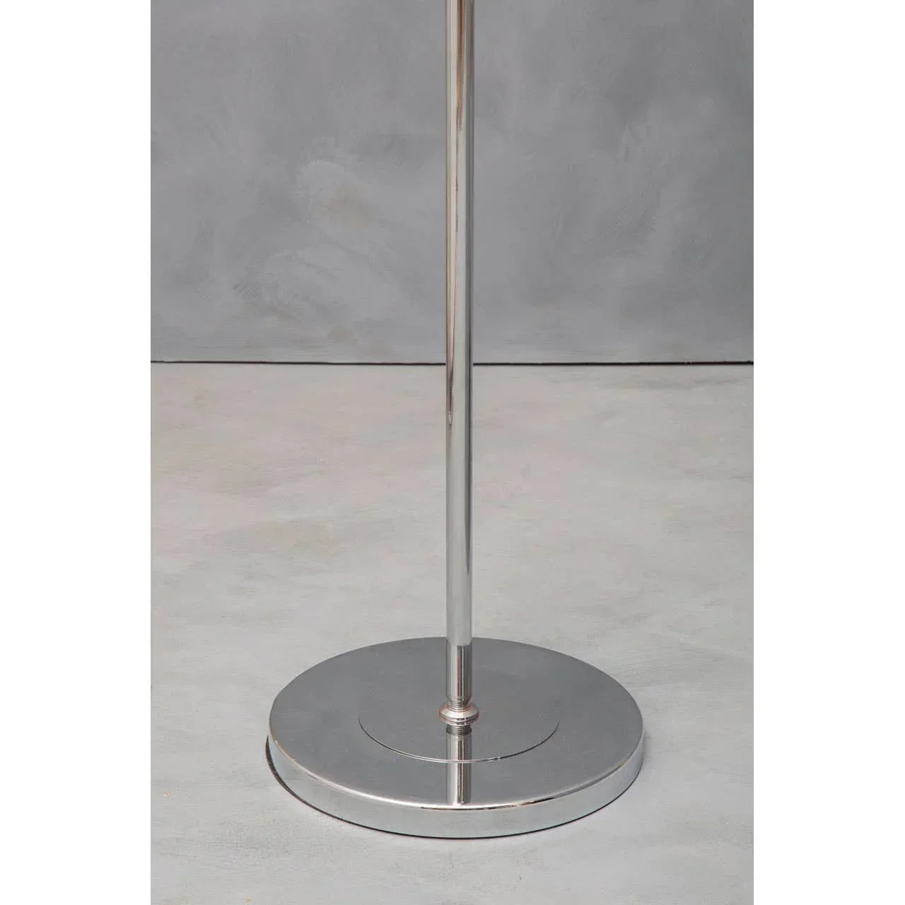 Chrome lamp base with round metallic stand on grey floor and backdrop