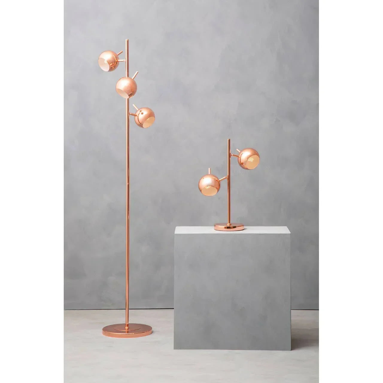 Copper finish floor lamp and matching table lamp with globe shades on grey background