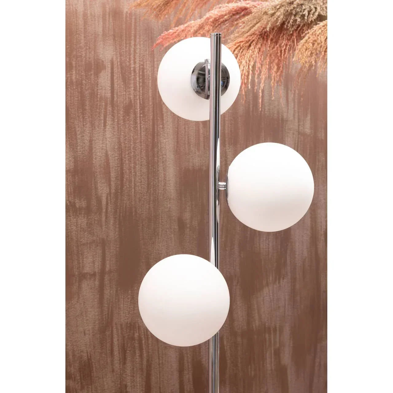 Modern floor lamp with three white glass globes on chrome stand against textured brown wall