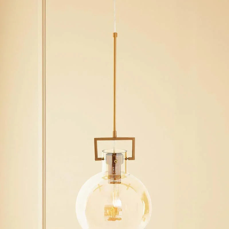 Glass globe pendant light with gold metal rod and exposed bulb against neutral wall