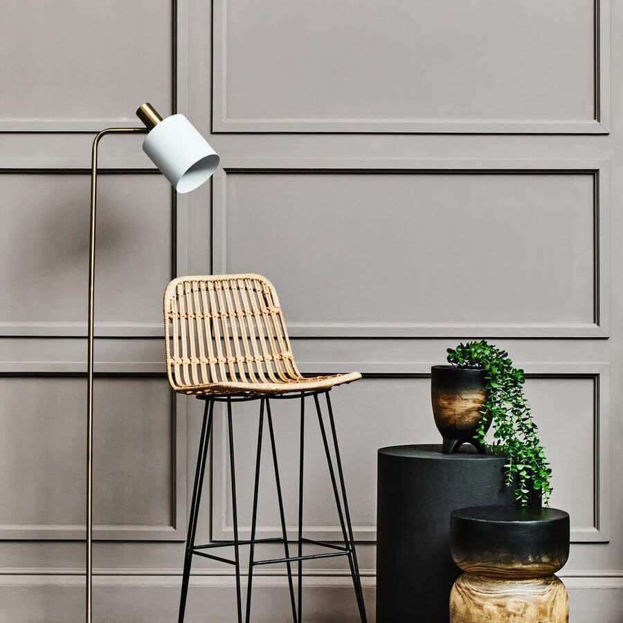 Rattan bar stool with metal legs beside modern side tables and indoor floor lamp