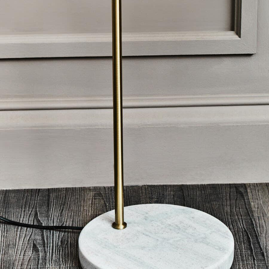 Brass floor lamp with white marble base on dark wood flooring