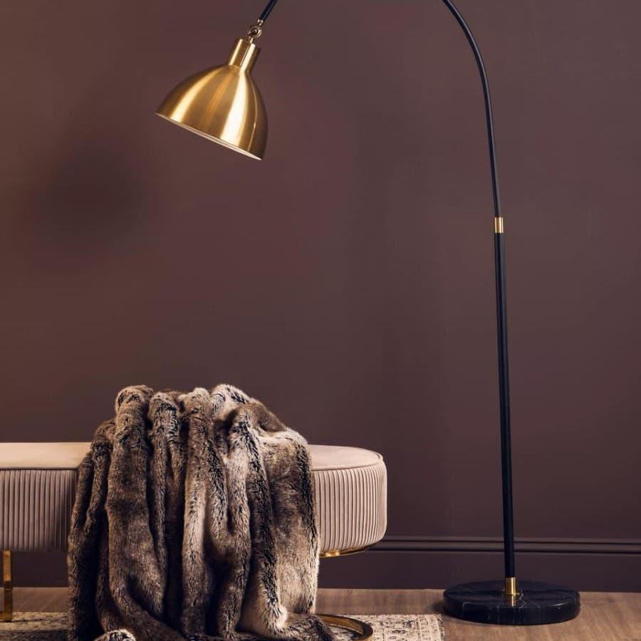 Gold floor lamp with black curved stand beside beige bench and faux fur throw on rug